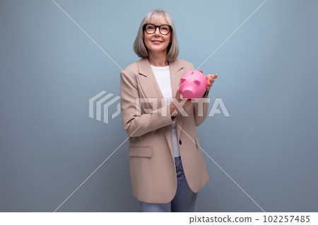 pleasant 60s middle-aged woman with a piggy bank of money on a bright background with copy space 102257485