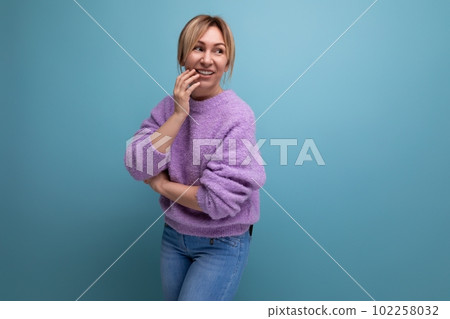 portrait of a charming pleasant blond young woman in a purple sweater on a blue background with copy 102258032