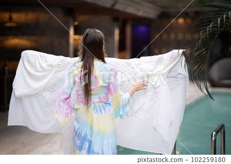 a female model portrays a movie star looks into the camera and poses in a white dress with angel wings on a summer veranda 102259180