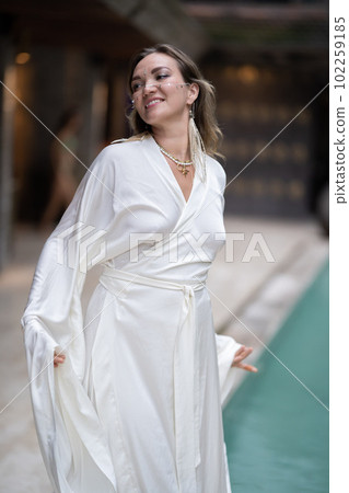 A model girl looks into the camera and poses in a white dress on a summer veranda, a beauty salon model 102259185