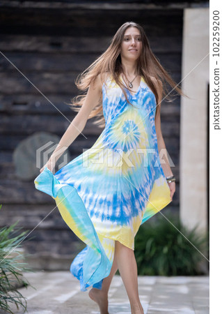 A young beautiful woman model is smiling, a young woman is walking down the street, her dress is blowing in the wind 102259200