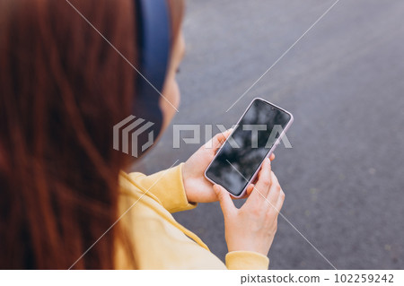 Woman listening music on earphones in the morning. Close-up image of hands using smartphone, searching or social networks concept, hipster typing a message to friends. For Graphic display montage Woman listening music on earphones in the morning. Close-up image of hands using smartphone, searching or social networks concept, hipster typing a message to friends. For Graphic display montage 102259242