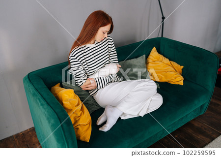 High-angle view of thoughtful young woman with broken hand wrapped in white plaster bandage sitting on sofa in apartment. Attractive redhead female with broken arm from accident at home alone. High-angle view of thoughtful young woman with broken hand wrapped in white plaster bandage sitting on sofa in apartment. Attractive redhead female with broken arm from accident at home alone. 102259595