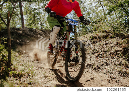 male racer cyclist riding dusty trail downhill race in forest, summer mountainbike championship 102261565