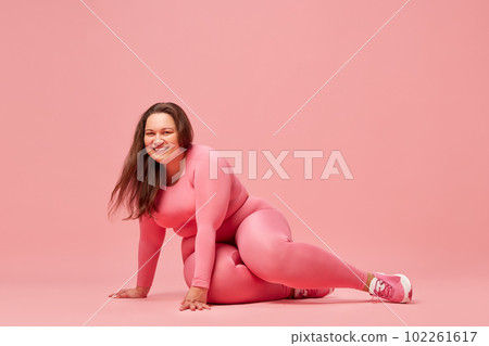 Self-care and well being. Young overweight woman training in sportswear against pink studio background Self-care and well being. Young overweight woman training in sportswear against pink studio background 102261617
