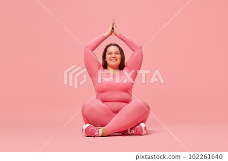 Yoga and meditation, wellness. Young overweight woman training in sportswear against pink studio background Yoga and meditation, wellness. Young overweight woman training in sportswear against pink studio background 102261640