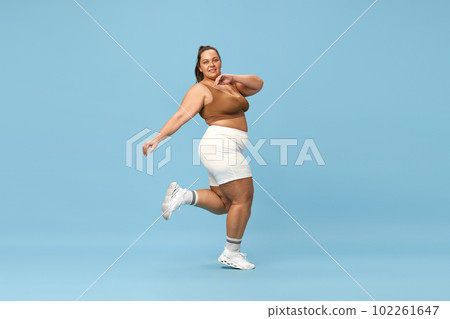 Active lifestyle and loss of calories. Young overweight woman training in sportswear against blue studio background 102261647
