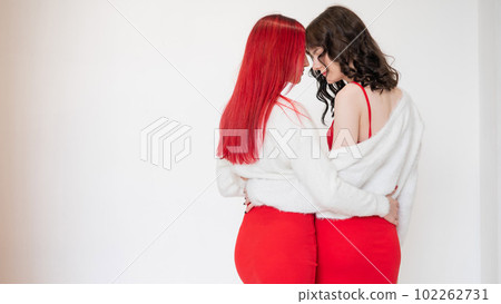 Rear view of two women dressed in identical red dresses and white sweaters. Lesbian intimacy. White background. 102262731
