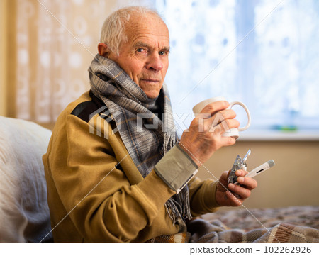 gray haired elderly man is sick and drinking hot tea at home 102262926