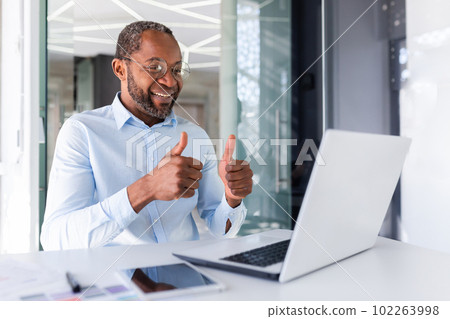Video call on online meeting, african american businessman boss talking to colleagues partners showing laptop camera thumbs up satisfied with team work achievement results. Video call on online meeting, african american businessman boss talking to colleagues partners showing laptop camera thumbs up satisfied with team work achievement results. 102263998