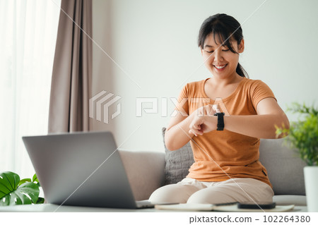 young woman looking and using a smartwatch, Female sitting on the sofa checking her smartwatch. young woman looking and using a smartwatch, Female sitting on the sofa checking her smartwatch. 102264380