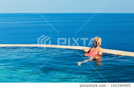 Girl at edge of infinity swimming pool with sea view. 102264405