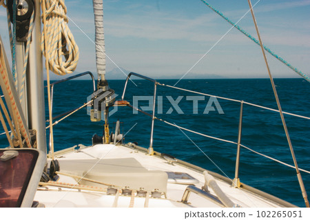 A sea voyage on a sunny, warm day. The bow of a yacht ship, ship's ropes. Yachting, nautical tourism. Marine landscape. The hills against blue sky and blue sea ocean water. Summer holidays trip. A sea voyage on a sunny, warm day. The bow of a yacht ship, ship's ropes. Yachting, nautical tourism. Marine landscape. The hills against blue sky and blue sea ocean water. Summer holidays trip. 102265051