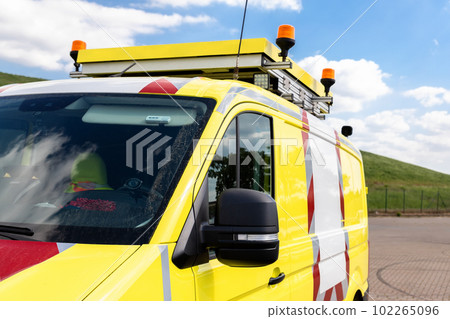 Yellow special cargo escort road traffic car roof mounted digital sign board. Repair and service van with ladder and orange light bar on roof at city street. Assistance or installation team vehicle 102265096
