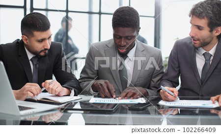 three colleagues of modern work co-working space talking and smiling while sitting at the desk table with laptop computer 102266409