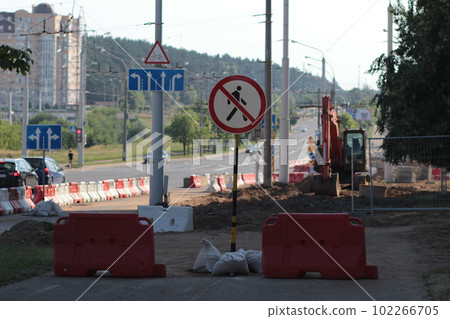 Construction work in the city in summer. Wide road repair. Warning road sign, barriers and excavator  102266705