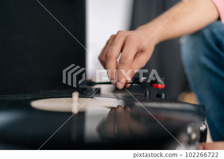 Close-up hands of unrecognizable young man adjusting head old record player and vinyl discs. Music lover male listening to classical music at home. Hipster guy listening to music on vinyl player. 102266722