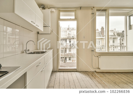 a kitchen with white cabinets and wood flooring in the middle, looking out onto an open door that leads to a balcony 102266836