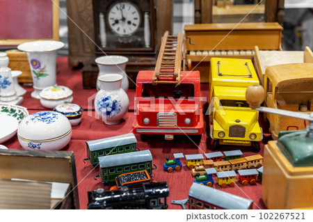 Pile of many colorful collectible scale retro car trucks wooden models, tableware, porcelain at street flea market. Second hand old vintage used item sale European traditional weekend market square Pile of many colorful collectible scale retro car trucks wooden models, tableware, porcelain at street flea market. Second hand old vintage used item sale European traditional weekend market square 102267521