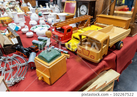 Pile of many colorful collectible scale retro car trucks wooden models, tableware, porcelain at street flea market. Second hand old vintage used item sale European traditional weekend market square Pile of many colorful collectible scale retro car trucks wooden models, tableware, porcelain at street flea market. Second hand old vintage used item sale European traditional weekend market square 102267522