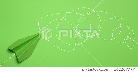 A green paper airplane on a green background with a long and convoluted path drawn, representing the concept of confusion, perplexity, and the difficulty of the journey A green paper airplane on a green background with a long and convoluted path drawn, representing the concept of confusion, perplexity, and the difficulty of the journey 102267777