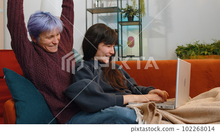 Celebrating Success: Two Lesbian Women Family Couple Use Laptop, Win Triumph, Good News at Home 102268014