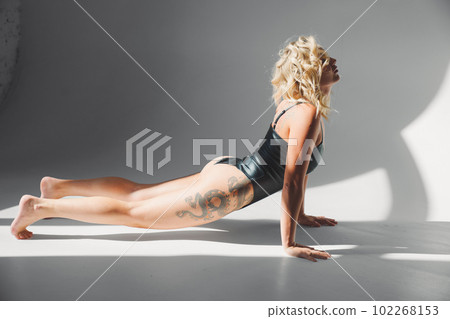 a sexy blonde with tattoos in a leather swimsuit performs sports exercises a sexy blonde with tattoos in a leather swimsuit performs sports exercises 102268153