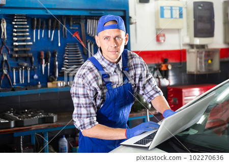 Mechanic with laptop near car engine in auto service Mechanic with laptop near car engine in auto service 102270636