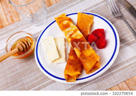 Thin crepes with slices of soft brie, honey and raspberries 102270654