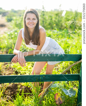 Happy young woman in summer clothes posing at the fence of farm 102270660