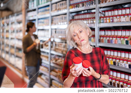 Elderly woman chooses bottles of paint in shop Elderly woman chooses bottles of paint in shop 102270712