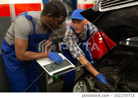Two auto mechanics diagnosing car engine with laptop Two auto mechanics diagnosing car engine with laptop 102270713