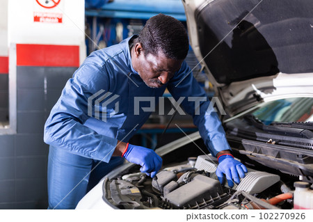 Professional american mechanic man in uniform repairing car engine 102270926