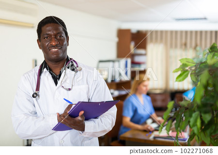 Positive african american male doctor writes important notes on a folder of documents Positive african american male doctor writes important notes on a folder of documents 102271068