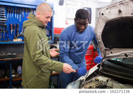 Worried client talking with specialist about repairing his car engine at workshop Worried client talking with specialist about repairing his car engine at workshop 102271136