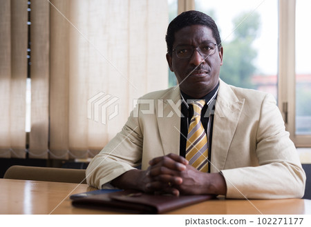 Portrait of friendly businessman at negotiation table in office Portrait of friendly businessman at negotiation table in office 102271177