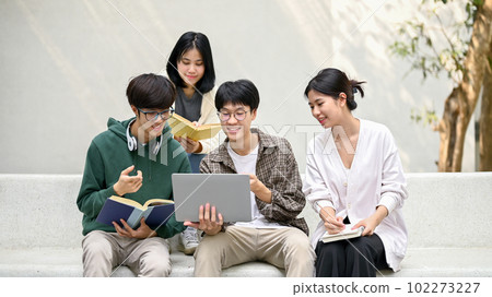 Group of happy young Asian college students sitting on a bench, looking at a laptop screen 102273227