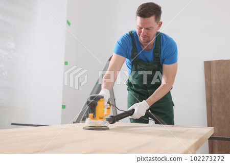 Carpenter polishes wooden table with modern grinder machine Carpenter polishes wooden table with modern grinder machine 102273272