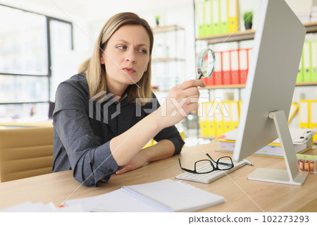 Curious woman looks at computer through magnifier glass Curious woman looks at computer through magnifier glass 102273293