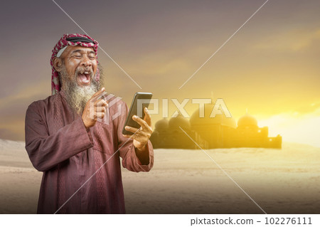 Muslim man with a beard wearing keffiyeh with agal using mobile phone 102276111