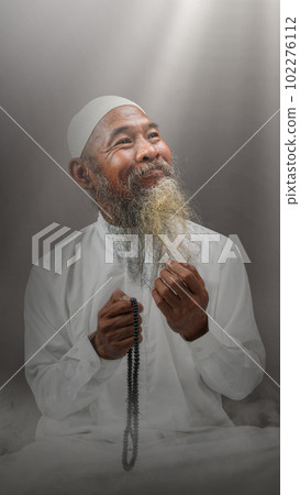 Muslim man with a beard wearing a white cap praying with prayer beads on his hands Muslim man with a beard wearing a white cap praying with prayer beads on his hands 102276112