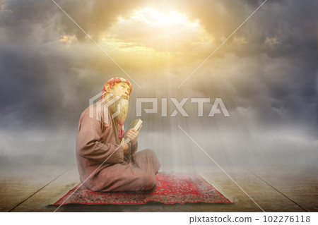 Muslim man with a beard wearing keffiyeh with agal holding Quran and prayer beads on his hands 102276118