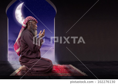 Muslim man with a beard wearing keffiyeh with agal in praying while raised hands Muslim man with a beard wearing keffiyeh with agal in praying while raised hands 102276130