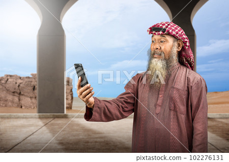 Muslim man with a beard wearing keffiyeh with agal using mobile phone Muslim man with a beard wearing keffiyeh with agal using mobile phone 102276131
