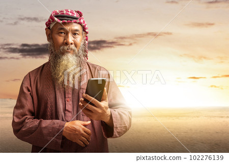 Muslim man with a beard wearing keffiyeh with agal using mobile phone 102276139