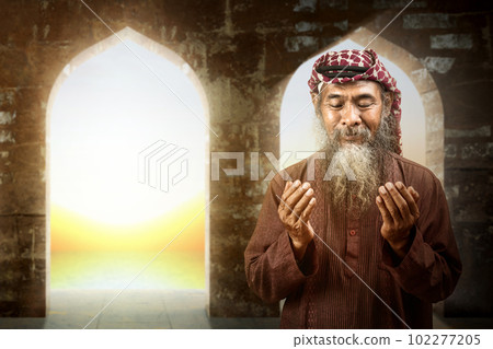 Muslim man with a beard wearing keffiyeh with agal in praying while raised hands Muslim man with a beard wearing keffiyeh with agal in praying while raised hands 102277205