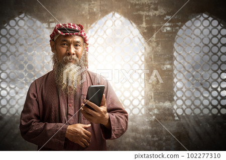 Muslim man with a beard wearing keffiyeh with agal using mobile phone 102277310