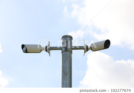 Public surveillance cameras mounted on a post with blue sky background 102277674