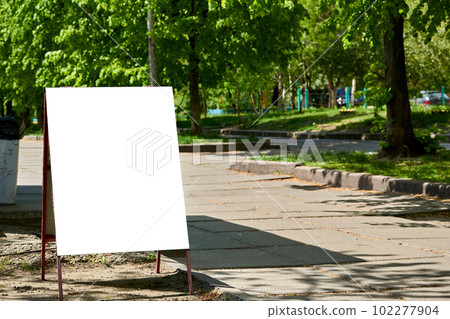 White poster banner billboard on the street with green trees, warm sunny day 102277904