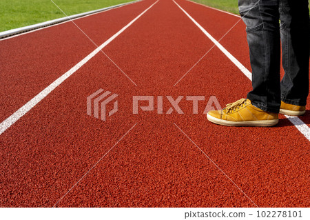 Man in brown sneakers and black jeans standing on a red running track Man in brown sneakers and black jeans standing on a red running track 102278101